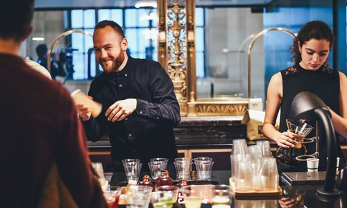 man and woman behind a bar, mixing drinks for their customers